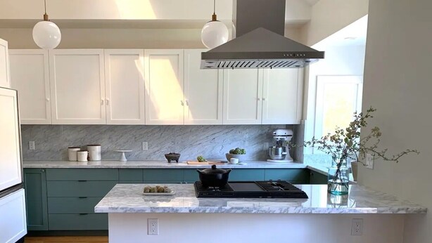 Une cuisine moderne avec des meubles blancs, un plan de travail en marbre, un îlot central doté de tabourets et un éclairage suspendu.