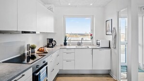 Een moderne keuken met witte kasten, een roestvrijstalen afzuigkap, een koffiezetapparaat, een magnetron en uitzicht op het buitenland door een groot raam.