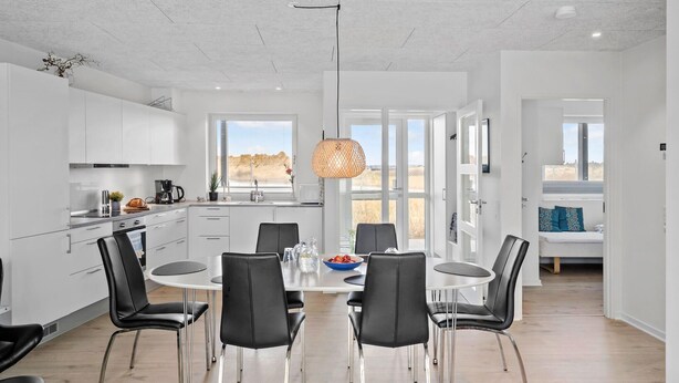 Een moderne keuken met witte kasten, een eethoek met een ronde tafel en zwarte stoelen, en een groot raam met uitzicht op de omgeving.
