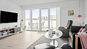 Een moderne woonkamer met een flatscreen televisie, een bank, een salontafel en een balkon met stoelen.
