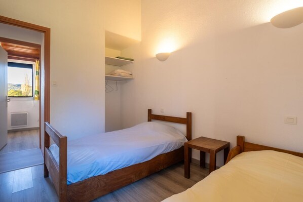 A small, single-bed room with a wooden headboard, a bedside table, and a built-in shelf above the bed.