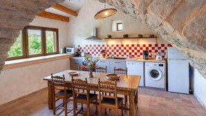 A rustic kitchen with stone walls, a checkered backsplash, wooden furniture, and a view through a window. - Gîte Aulas 2/4 Pers - LA Tieule (LA TIEULE)