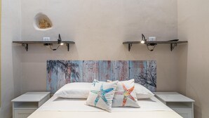 A bedroom with a bed, two bedside tables, a headboard with a painted mural, and two wall-mounted shelves with lights. - Lukìa House in the heart of Syracuse (Siracusa)