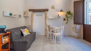 A cozy living area with a grey sofa, a small table with chairs, a coffee machine, and a wooden cabinet. - Lukìa House in the heart of Syracuse (Siracusa)