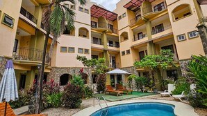 A multi-story hotel with a swimming pool, outdoor seating, and lush landscaping.