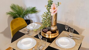 Une table à manger dressée avec de l’argenterie blanche, des couverts et des verres, le tout disposé autour d’un vase décoratif contenant des fleurs et des plantes.