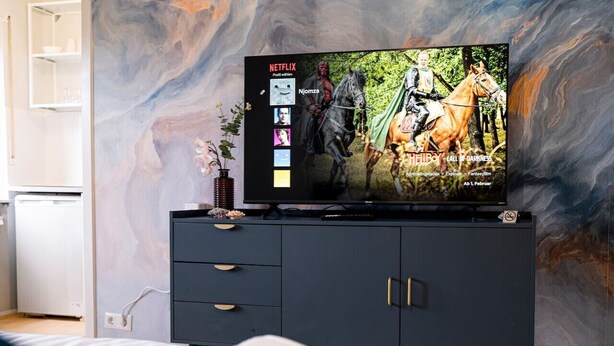 Une chambre à coucher avec un lit, un téléviseur posé sur un meuble noir et un mur en marbre.
