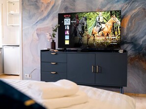 Une chambre à coucher avec un lit, un téléviseur posé sur un meuble noir et un mur en marbre.