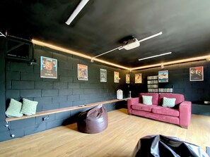 Une pièce avec un mur en briques sombres, un banc en bois, un canapé rouge et un projecteur fixé au plafond.