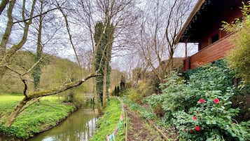 Un jardin avec un étroit canal d’eau, des arbres et un bâtiment en bois.