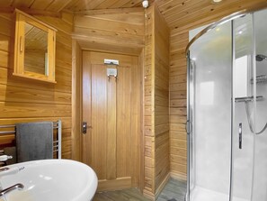 Een badkamer met houten lambrisering, een wastafel, spiegel en een douche met glazen wanden.