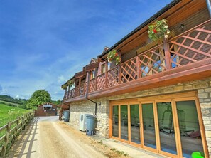 Een gebouw met twee verdiepingen, een gevel van natuursteen, houten balkonleuningen en grote glazen deuren.