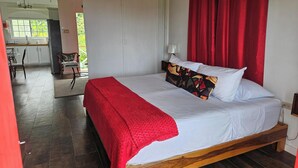 Camera da letto con un letto, tende rosse, una testiera in legno e vista su cucina e sala da pranzo.