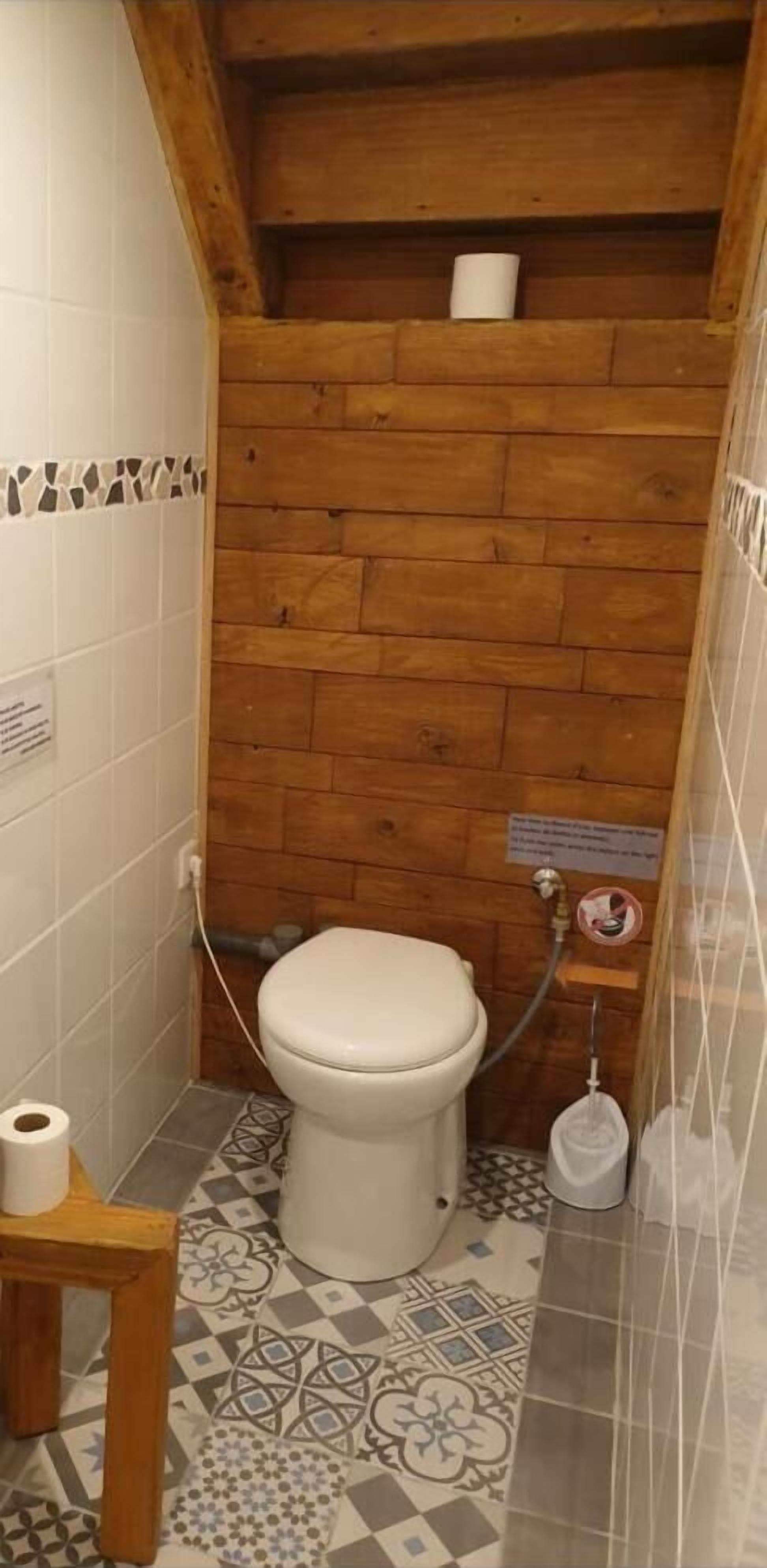 Une petite salle de bain compacte avec un plafond en bois, des toilettes, une douche et des carreaux de sol à motifs.