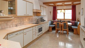 A compact kitchen with a dining area, featuring a built-in oven, a sink, and a dining table with chairs. - Apartment mit Bergblick (Aschau im Zillertal)