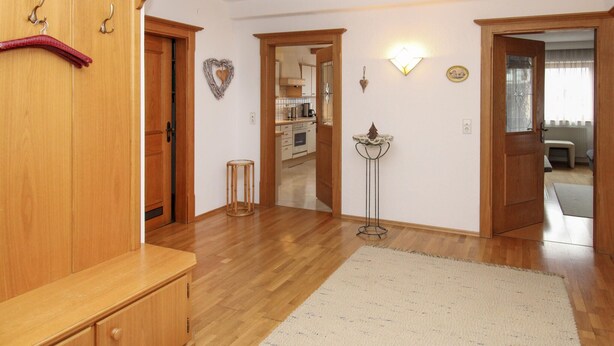 A spacious living area with wooden flooring, a large rug, and a kitchen visible through an open doorway. - Apartment mit Bergblick (Aschau im Zillertal)