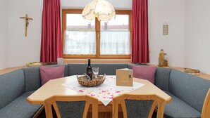 A cozy dining area with a wooden table, grey upholstered chairs, and a window with red curtains. - Apartment mit Bergblick (Aschau im Zillertal)