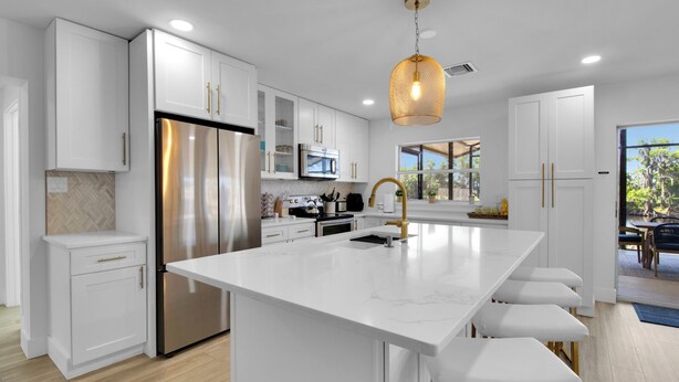A modern kitchen with white cabinetry, stainless steel appliances, and a central island with bar stools. - Gorgeous St. Johns River home 3bdrm/2 bth (Osteen)