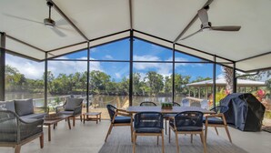 A spacious outdoor patio with a large table and chairs, surrounded by large windows offering a view of a lake and greenery. - Gorgeous St. Johns River home 3bdrm/2 bth (Osteen)