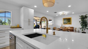 A modern kitchen with white cabinetry, a large island with a sink, and a dining area with wicker furniture. - Gorgeous St. Johns River home 3bdrm/2 bth (Osteen)