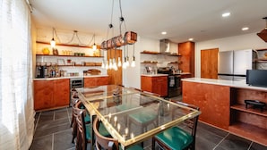 Una cocina moderna con una mesa de comedor de cristal, armarios de madera e iluminación colgante.