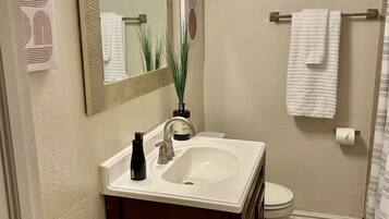 Een badkamer met een wit wastafel, een donker houten opbergmeubel, een spiegel met gouden lijst, een toilet en een douchegordijn.