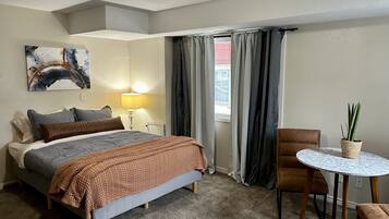Een hotelkamer met een bed, een bedlamp, een kleine tafel met een plant en een raam met gordijnen.