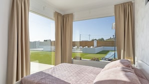 Ein Schlafzimmer mit einem großen Fenster, einem Bett mit gesteppter Bettdecke und Vorhängen.
