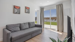 Ein modernes Wohnzimmer mit einem grauen Sofa, zwei gerahmten Kunstwerken, einem Flachbildfernseher und einer Schiebeglasdoor zum Außenbereich.
