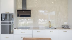 Eine moderne Küche mit Edelstahlgeräten, einer Marmor-Spritzschutzwand und einem Holztisch.