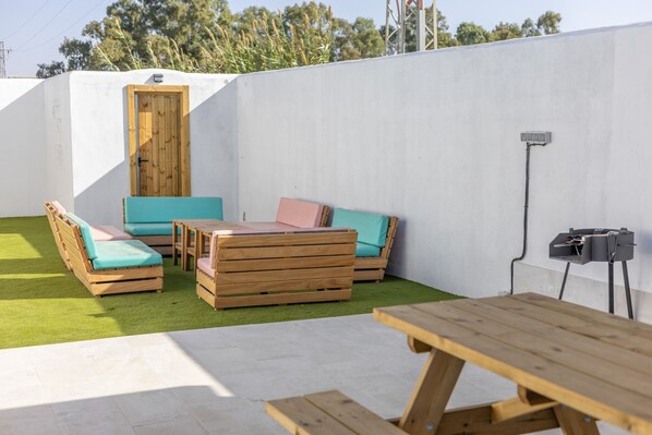 A patio area with wooden furniture, a table, and a white wall with a door.