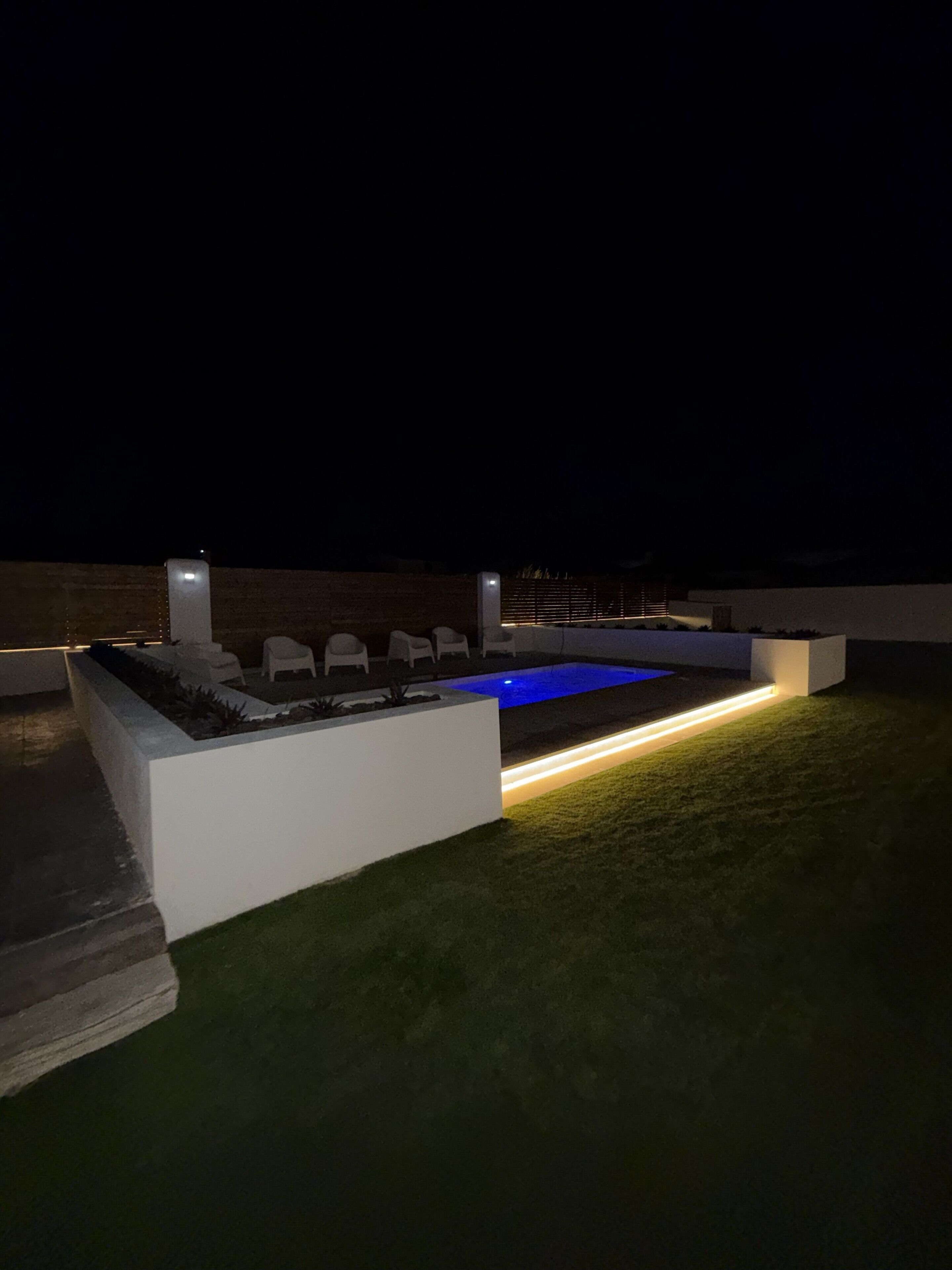 Un espace piscine doté d’une piscine rectangulaire, de chaises longues blanches et d’un petit muret.