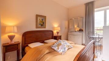 Een slaapkamer met een houten bed, twee bedlampen, een nachtkastje, een kleine tafel, een stoel, een spiegel en een raam met gordijnen.