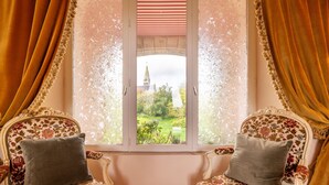 A room with two ornate chairs, a window with a view of a church, and a patterned curtain. - Castle 'Gite La Renardière' with Private Pool, Private Terrace and Wi-Fi (Langoëlan)