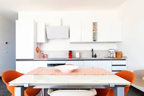 Une cuisine moderne avec des meubles blancs, une table à manger avec des chaises orange et une machine à café.