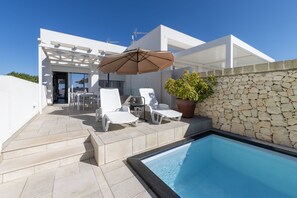 Un área de piscina moderna al aire libre con sillones de descanso, una pérgola y un muro de piedra.