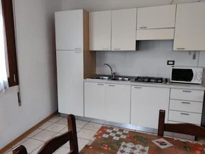 Eine kleine Küche mit weißen Schränken, einer Spüle, einem Herd und einer Mikrowelle.