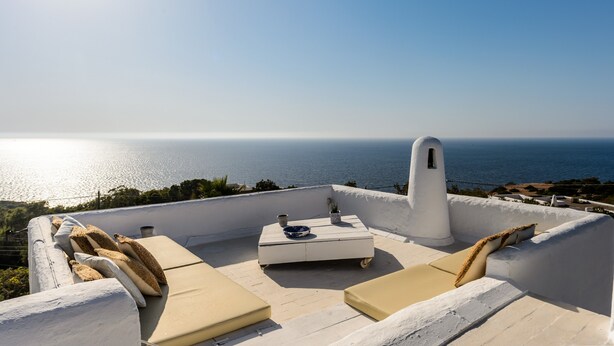 Eine Dachterrasse mit Blick auf das Meer, ein weißer Tisch mit einer Schale und ein Blumentopf.