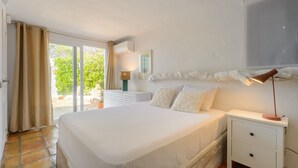 Ein Schlafzimmer mit einem großen Bett, einem Nachttisch, einer Lampe, einem Fenster mit Vorhängen und einer Wand-Klimaanlage.