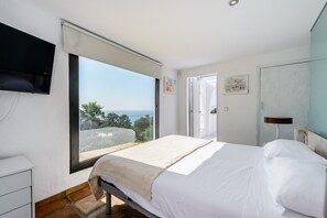 Un dormitorio con una ventana grande, una cama, un televisor y una puerta que da a un balcón.
