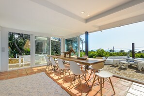 Un comedor moderno con una mesa larga, sillas blancas y un amplio ventanal que ofrece vistas al exterior.