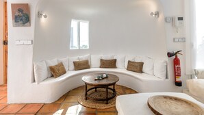 Ein modernes Wohnzimmer mit einem gebogenen weißen Sofa, einem runden Couchtisch und einem an der Wand befestigten Feuerlöscher.