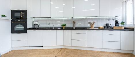 Une cuisine moderne avec des meubles blancs, un micro-ondes noir, une machine à café et un plancher en bois.