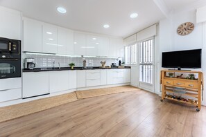 A modern kitchen with white cabinets, a black oven, a wooden wine rack, and a TV on the wall.