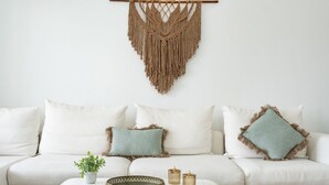 A white sofa with two pillows, a macrame wall hanging, a small plant, and two candle holders on a white table. - Villa 'Casa Ohana' with sea views, Wi-Fi, and air conditioning (Fuengirola)