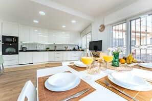 A modern kitchen with white cabinets, a black oven, and a dining area with white plates, cutlery, and a glass of orange juice.