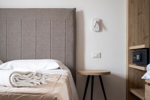 Een hotelkamer met een bed, nachtkastje, een op de muur bevestigde thermostaat en een ingebouwde magnetron.