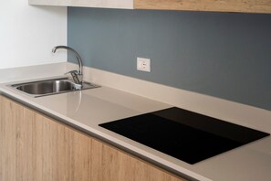 Een moderne keuken met een roestvrijstalen spoelbak, een zwart inductiekookveld en houten kastjes.