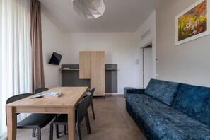 Een moderne woonkamer met een houten eettafel, zwarte stoelen, een blauwe bank, een flatscreen televisie en een keukenhoek.