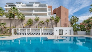 Una piscina con sillas de descanso, palmeras y un edificio moderno con balcones.